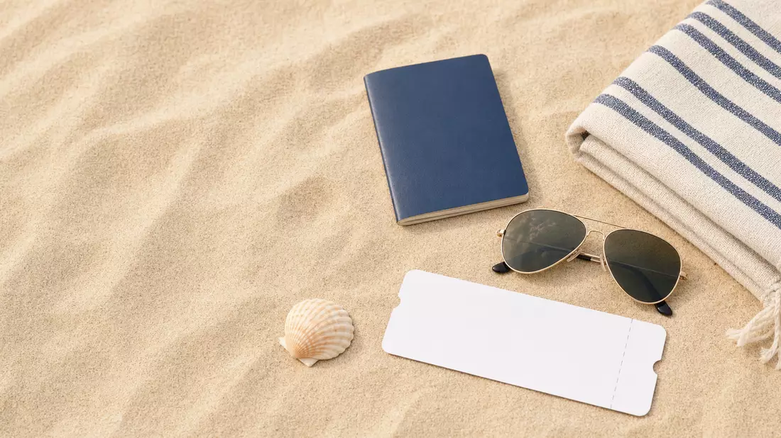 Vogelperspektive auf Reiseutensilien: Pass, Sonnenbrille, Strandtuch und Ticket auf Sand
