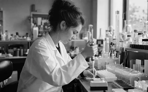 Novo Nordisk A/S (DK0062498333): Forscherin im Labor-Kittel bedient Pipette in dokumentarischem Schwarzweiß-Reportagefoto - Foto: THN