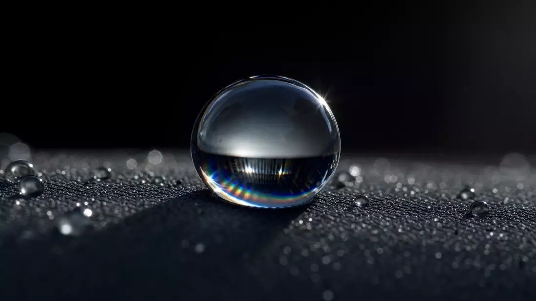 Extreme Makro-Aufnahme eines Wassertropfens auf hydrophober Oberfläche mit Regenbogenreflexion