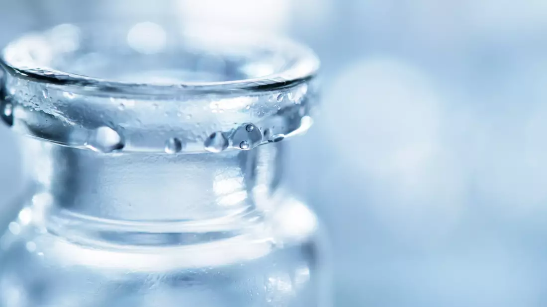 Extreme Makro-Nahaufnahme des Glasrands eines Pharma-Vials mit Wassertropfen