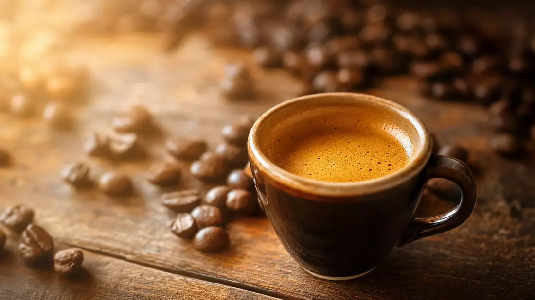 Espressotasse mit Crema auf Holztisch, Kaffeebohnen im Hintergrund
