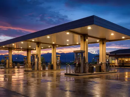 Shell plc GB00BP6MXD84: fotorealistische Tankstelle bei Abenddämmerung mit leuchtendem Vordach und nasser Vorfahrt - Foto: THN