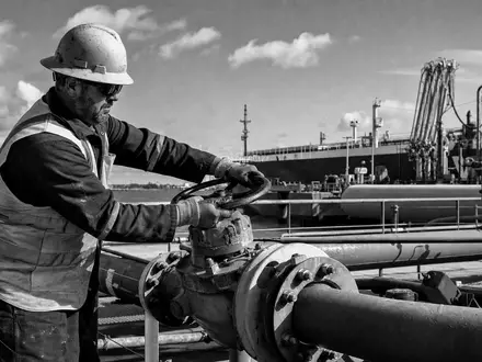 Shell plc GB00BP6MXD84: dokumentarische Schwarz-Weiß-Aufnahme eines Industriearbeiters mit Helm an einer Tanker-Verladestation - Foto: THN