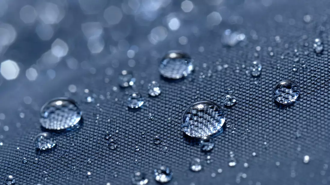 Extreme Nahaufnahme: Wassertropfen perlen auf dunkelblauem Regenschirmstoff