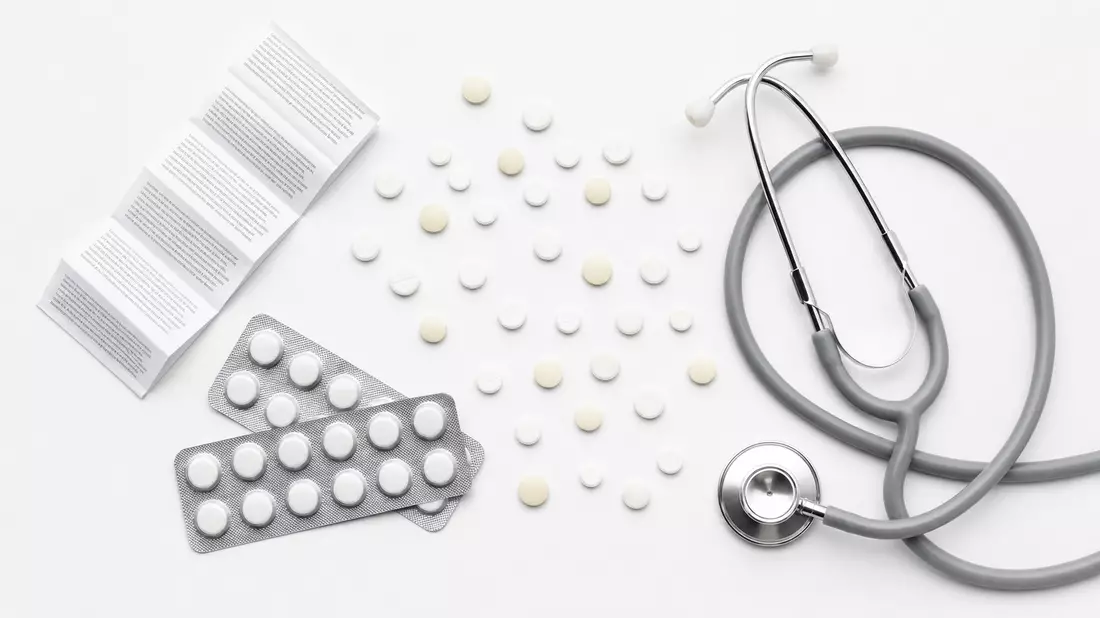 Draufsicht auf Tabletten, Blisterpacks, Beipackzettel und Stethoskop auf weißem Untergrund