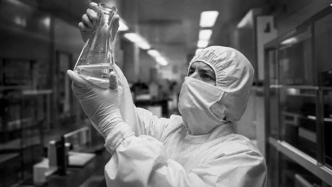 Forscher in weißem Reinraumanzug hält Glaskolben im Labor, Schwarz-Weiß