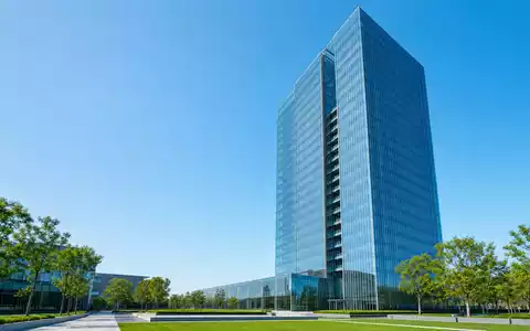 Roche Holding AG CH0012032048 – Schlanker Glas-Wolkenkratzer mit grünem Vorplatz unter blauem Himmel - Foto: THN
