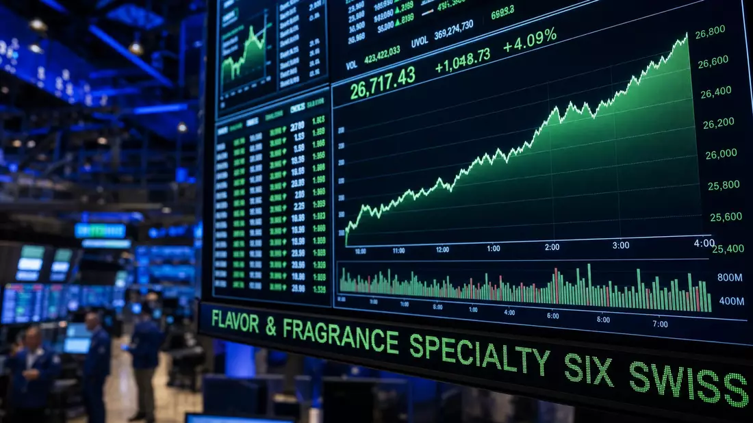 A financial editorial photograph of a large stock exchange monitor. The screen displays rising green financial charts and numeric price data. A bright green LED ticker banner reads FLAVOR & FRAGRANCE SPECIALTY SIX SWISS. The background shows a blurred tra
