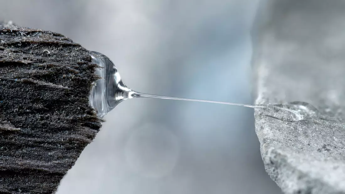 Extreme macro photo of a transparent adhesive glue drop stretching a thin viscous thread between two rough surfaces