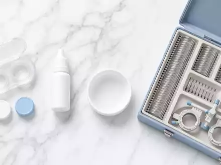 Alcon CH0432492467: Flatlay mit Kontaktlinsenbehälter, Pflegelösung und Probierlinsen Set auf weißem Marmor - Foto: THN