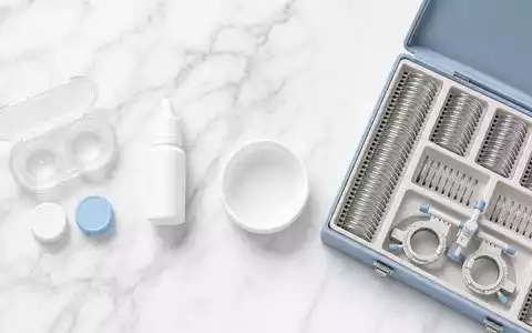 Alcon CH0432492467: Flatlay mit Kontaktlinsenbehälter, Pflegelösung und Probierlinsen Set auf weißem Marmor. - Foto: THN