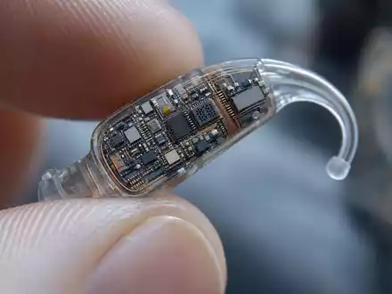 Sonova CH0012549785: Extreme Makro-Nahaufnahme eines winzigen Hi-Tech-Hörgeräts mit sichtbarer Mikroelektronik und transparentem Gehäuse - Foto: THN