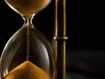 Swiss Life CH0014852781 Makro: goldene Sanduhr mit fließendem Sand und dramatischem Seitenlicht auf schwarzem Hintergrund - Foto: THN
