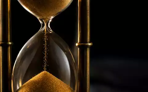 Swiss Life CH0014852781 Makro: goldene Sanduhr mit fließendem Sand und dramatischem Seitenlicht auf schwarzem Hintergrund - Foto: THN