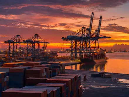 Kuehne Logistik CH0025238863: Containerhafen mit mächtigen Kränen und gestapelten Containern bei Abenddämmerung - Foto: THN