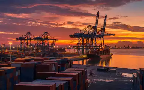 Kuehne Logistik CH0025238863: Containerhafen mit mächtigen Kränen und gestapelten Containern bei Abenddämmerung - Foto: THN