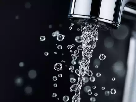 Geberit (CH0030170408) Makro-Detail zeigt einen Wasserstrahl und Tropfen an der glänzenden Chrom-Armatur - Foto: THN