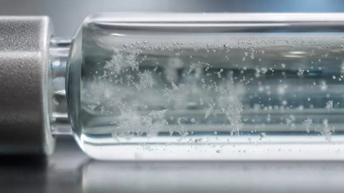 Extreme Makroaufnahme einer gefrorenen transparenten Flüssigkeit mit feinen Eiskristallen in einem Glasfläschchen