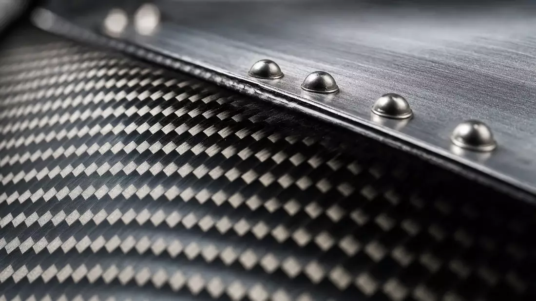 Makroaufnahme von Karbonfaser-Verbundwerkstoff mit Nieten und Metalltextur