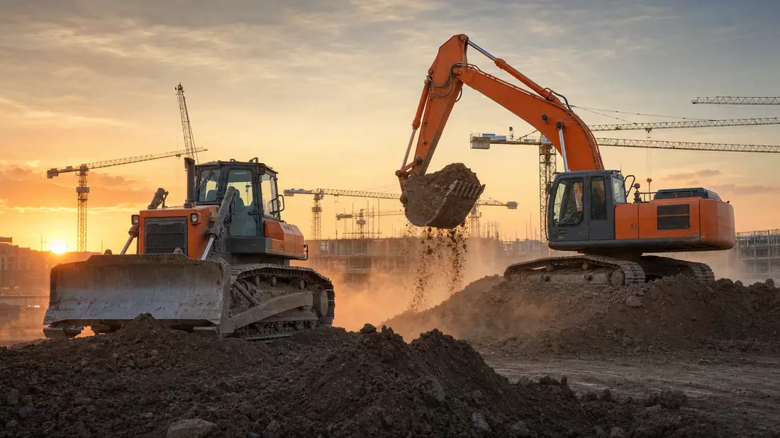 Bulldozer und Bagger auf Baustelle bei Sonnenuntergang, orange-graue Baumaschinen