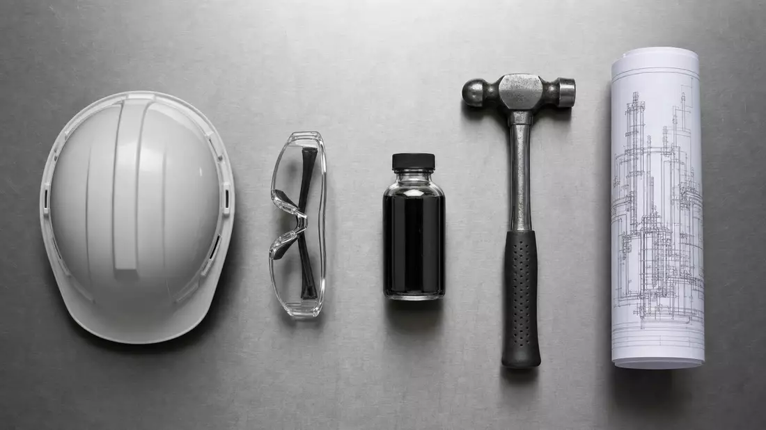 Overhead flat lay of oil industry tools on brushed steel: plain hard hat, safety goggles, crude oil sample bottle, steel hammer, and rolled engineering blueprint, evenly spaced with even studio lighting