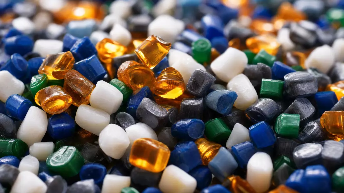 Extreme close-up macro photography of polymer plastic granule pellets in translucent amber, opaque white, deep blue, emerald green, and charcoal gray colors, each granule showing unique light refraction and surface texture, sharp focus on foreground with 
