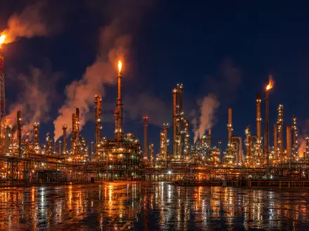Exxon US30231G1022 zeigt eine riesige Raffinerie mit Schornsteinen und Flackerflammen bei dramatischer Nacht - Foto: THN