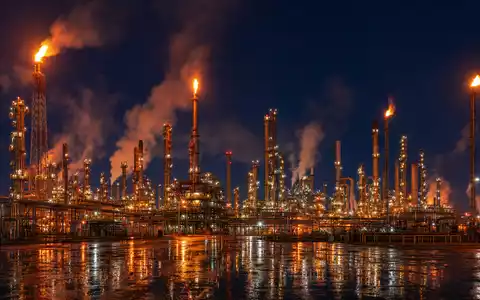 Exxon US30231G1022 zeigt eine riesige Raffinerie mit Schornsteinen und Flackerflammen bei dramatischer Nacht - Foto: THN