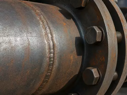 Exxon US30231G1022 im Makro: Pipeline-Stahlrohr mit deutlicher Schweißnaht und rostigen Flansch-Schrauben sichtbar - Foto: THN