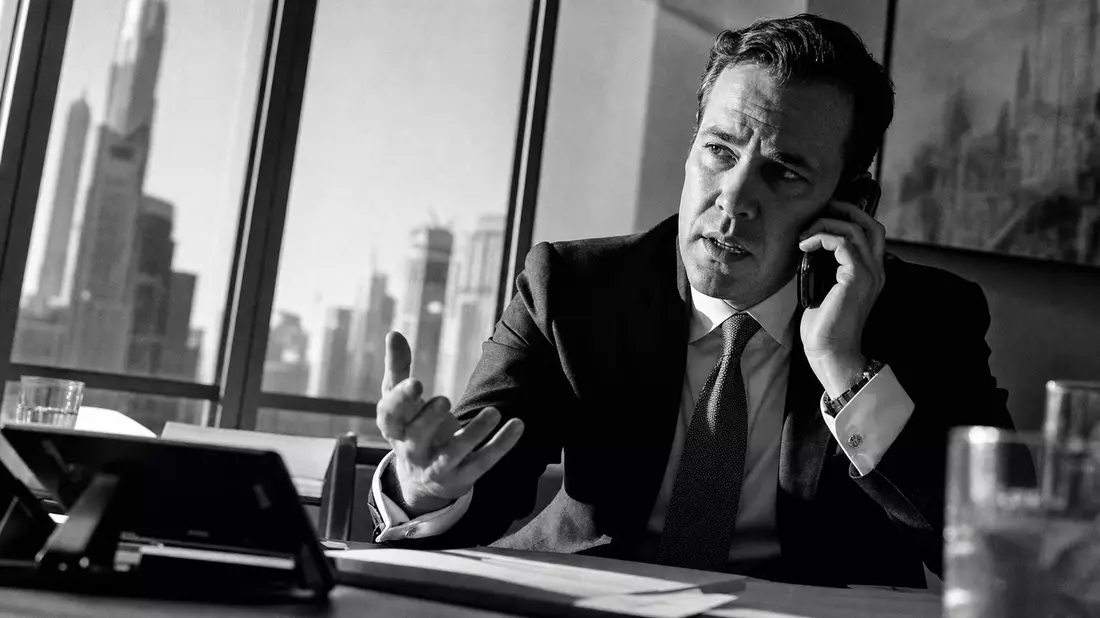 Black and white documentary photograph of an investment banker in a suit holding a smartphone to his