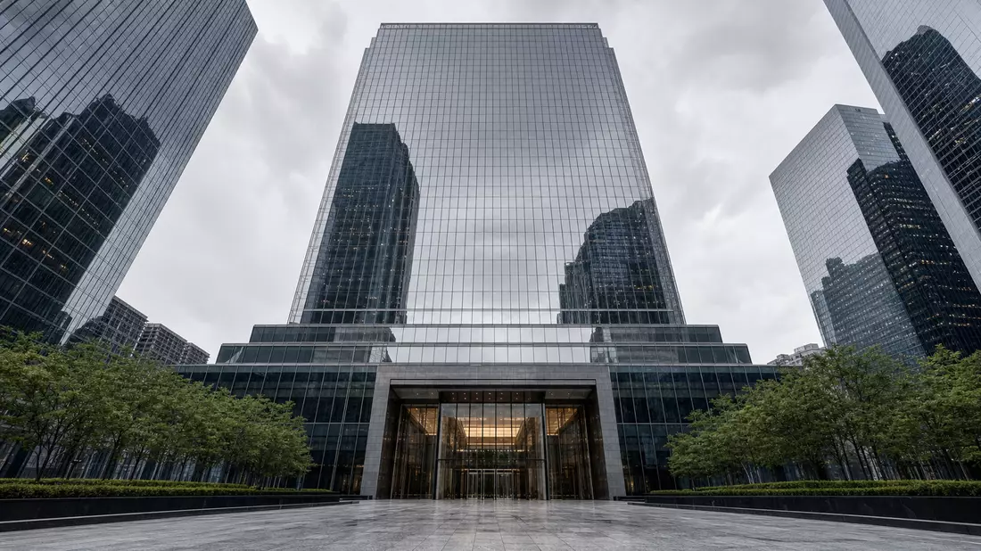 Low-angle architectural photography of a sleek modern investment bank headquarters glass tower in New York City, dark reflective curtain-wall facade mirroring the overcast sky, polished stone plaza with symmetrical entrance at base, flanked by other skysc