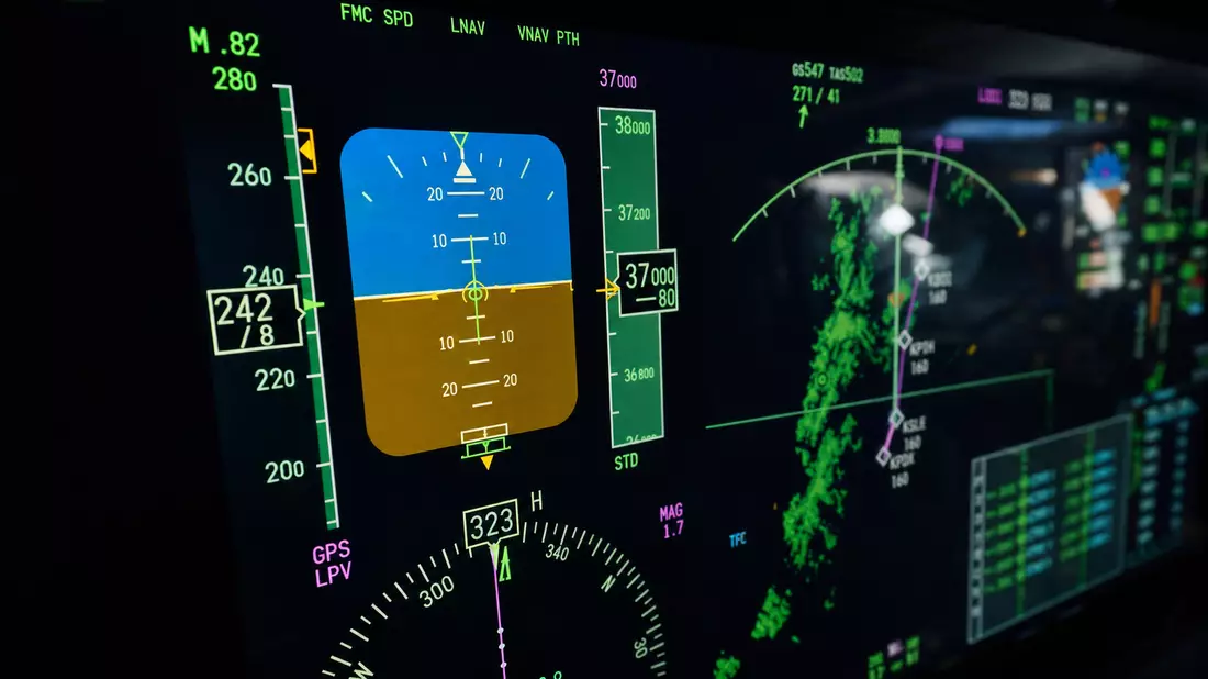Extreme macro close-up of aircraft avionics multifunction display screen showing detailed flight instruments including artificial horizon, altitude readout, airspeed, navigation waypoints, glowing green amber data on dark LCD, shallow depth of field