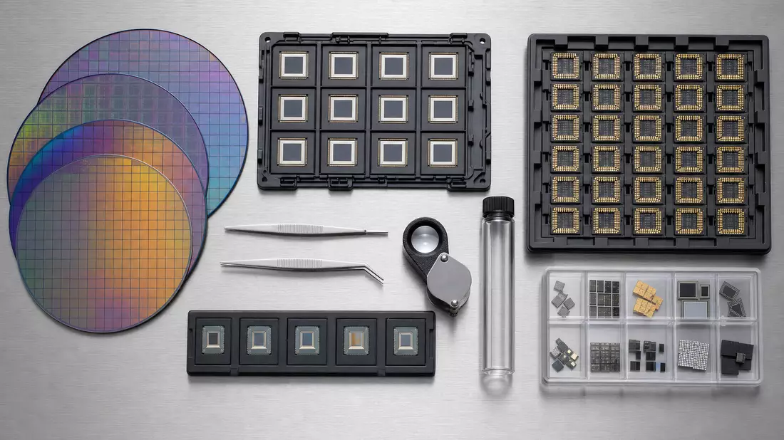 Top-down flatlay on brushed stainless steel of iridescent silicon wafers, chip carrier trays, precision tweezers, jeweler loupe, and glass sample tube arranged neatly under even studio lighting