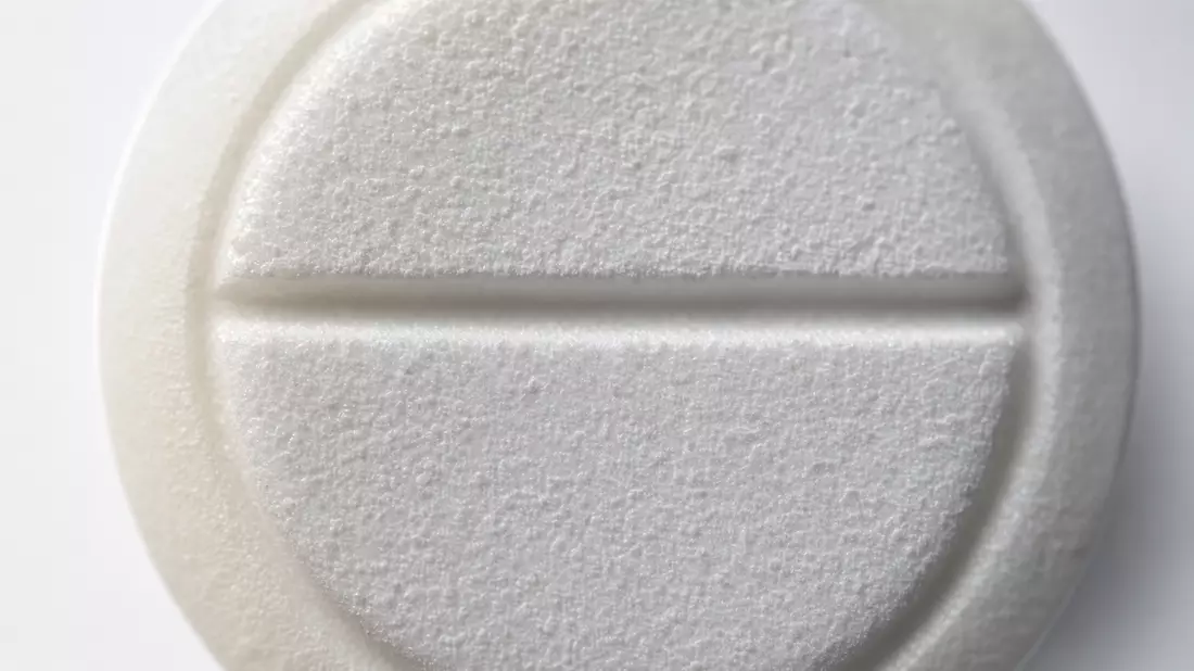 Extreme close-up macro photograph of a single white pharmaceutical tablet filling the entire frame. 