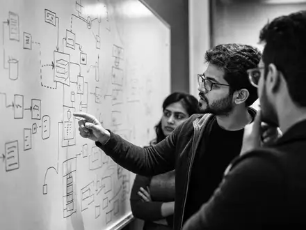 Microsoft Corporation (US5949181045) präsentiert Entwickler vor Whiteboard mit Architektur-Diagrammen im dokumentarischen Schwarz-Weiß - Foto: THN