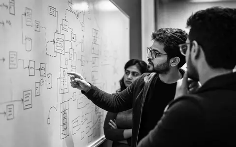 Microsoft Corporation (US5949181045) präsentiert Entwickler vor Whiteboard mit Architektur-Diagrammen im dokumentarischen Schwarz-Weiß - Foto: THN