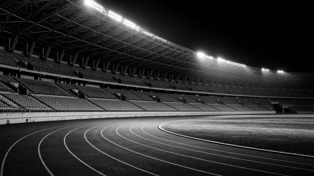 Schwarzweißes Stadion mit Laufbahn und Flutlicht in dokumentarischer Reportage-Ästhetik