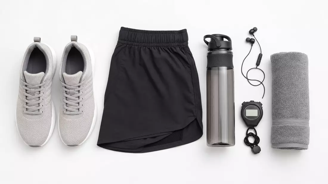Overhead-Flatlay von Sportausrüstung: Sneaker, Shorts, Trinkflasche und Stoppuhr auf Weiß