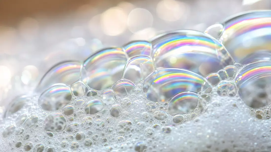 Extremes Makrofoto von irisierenden Seifenblasen und weißem Waschmittelschaum mit Regenbogenreflexen