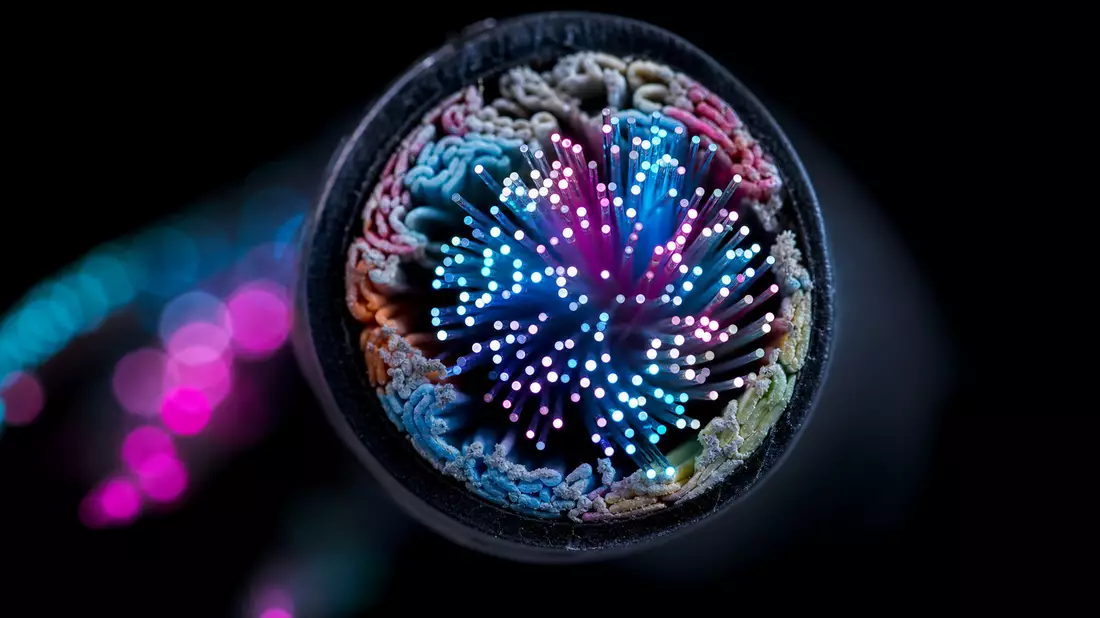 Extreme Makrofotografie des Querschnitts eines Glasfaserkabels, leuchtende Cyan- und Magenta-Lichtpunkte auf schwarzem Hintergrund, weiches Bokeh
