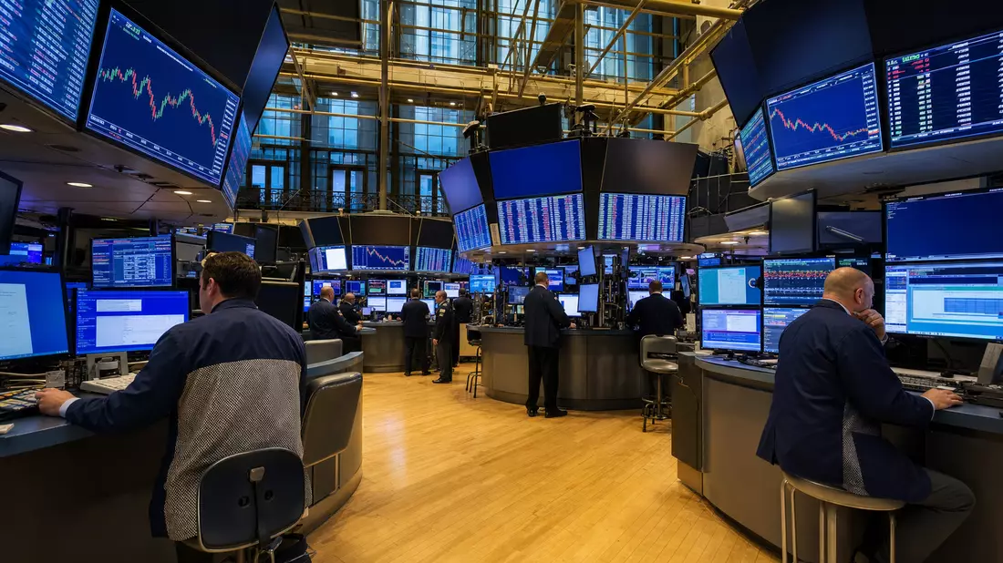 Redaktionelles Weitwinkelfoto des NYSE-Börsenparketts mit Händlern an Workstations und großen Kursanzeige-Bildschirmen, dramatische Beleuchtung