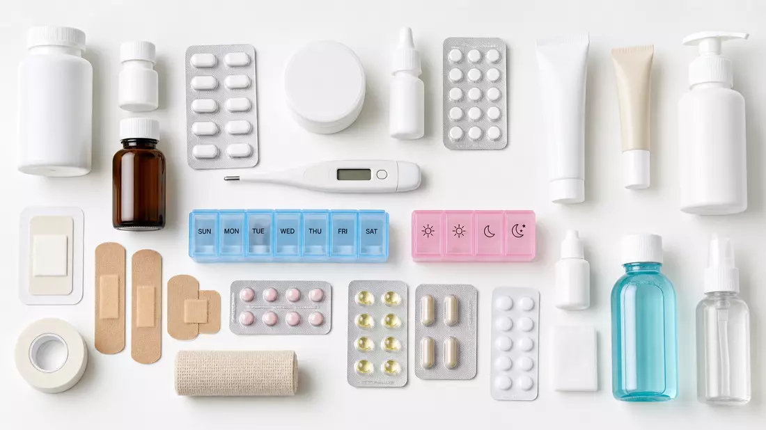 Draufsicht-Flatlay auf Apothekenprodukte: Tabletten-Blister, Medizinfläschchen, Pflaster, Thermometer und Cremebehälter auf weißer Fläche