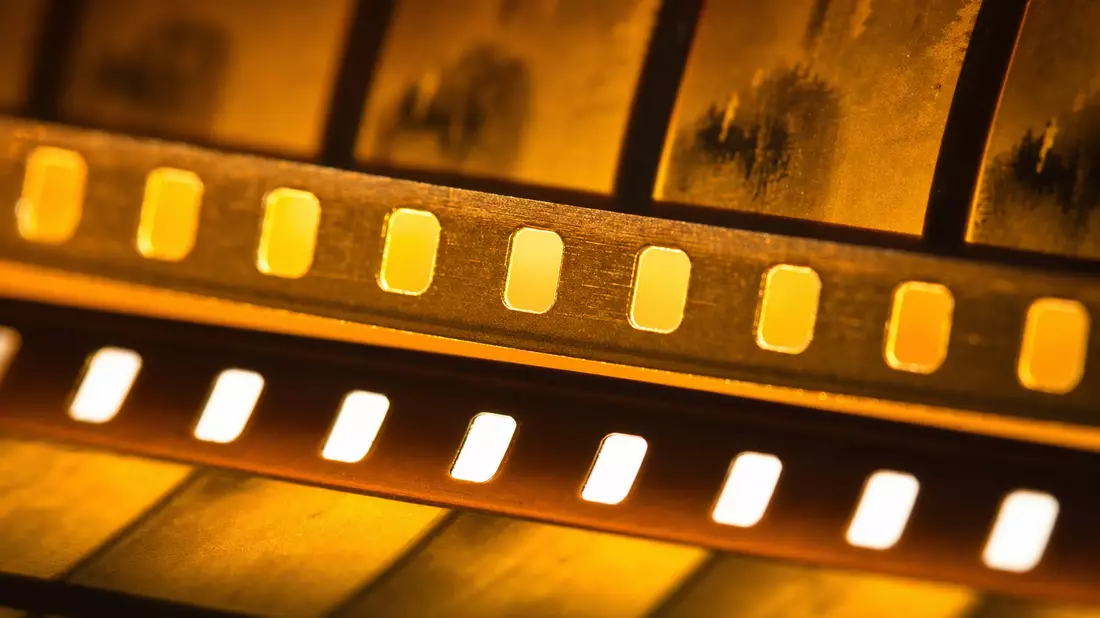 Extreme Makroaufnahme eines 35mm-Filmstreifens in goldenen Bernsteintönen, bei der Perforationslöcher scharf abgebildet und Filmrahmen mit schöner Tiefenschärfe verschwimmen
