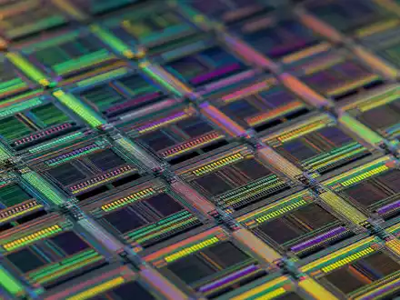 Broadcom Inc. (US11135F1012): detailreiche Makroaufnahme eines Halbleiter-Wafers zeigt feinste, schimmernde Mikrochip-Schaltkreisstrukturen in Nahaufnahme - Foto: THN