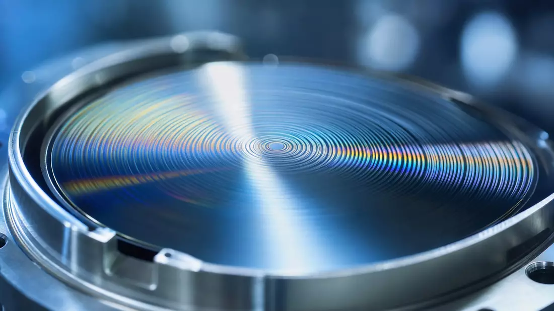 Extreme Makrofotografie einer hochpolierten EUV-Optikspiegelfläche mit sichtbaren Interferenzringen und irisierenden Reflexionen in Blau und Silber