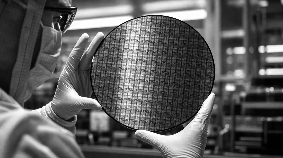 Schwarz-Weiß-Reportagefoto eines Technikers im Reinraum, der einen Silizium-Wafer mit hunderten Chip-Dies hält – dokumentarischer Stil, kein Markenname