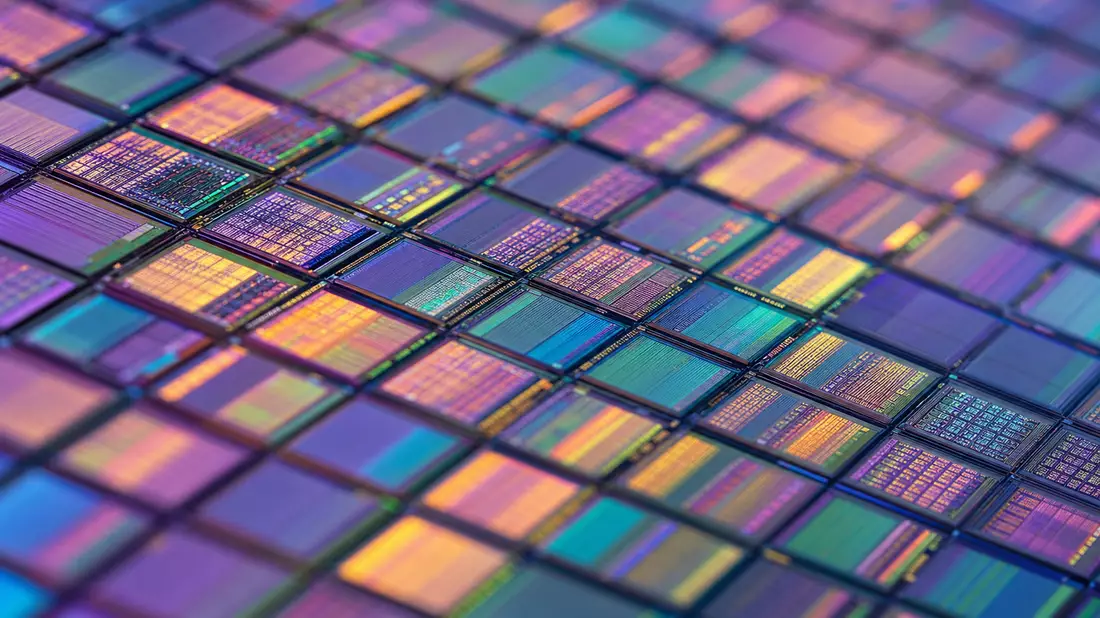 Extreme Makroaufnahme einer Silizium-Wafer-Oberfläche mit irisierenden Regenbogenfarben auf geometrischen Chip-Dies, violette und goldene Interferenzfarben, kein Markenname