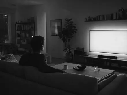 Netflix US64110L1061 dokumentiert einen anonymen Zuschauer auf Couch vor leuchtendem Bildschirm im SW-Reportagestil - Foto: THN