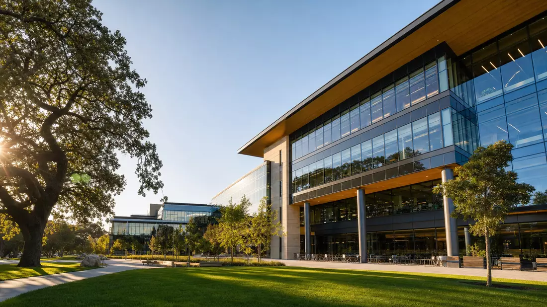 Architekturaufnahme eines modernen Tech-Campus-Gebäudes mit Glasfassade, Eichen und gepflegtem Rasen im goldenen Nachmittagslicht