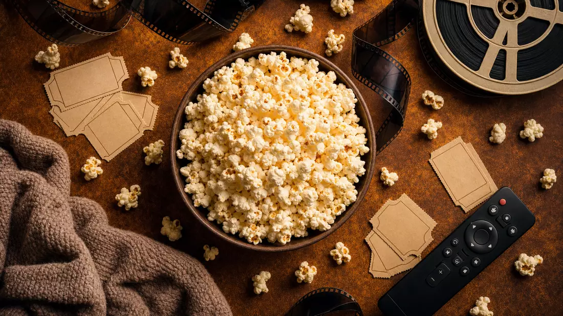 Flat-Lay-Draufsicht auf eine Filmabend-Arrangement mit Popcornschüssel, Filmstreifen, leeren Tickets und Fernbedienung auf warmem Hintergrund